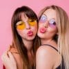 Couple of pretty girls with sunglasses and painted lips, best friends posing on pink background