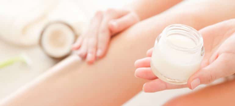 closeup of woman applying coconut cream moisturizer to legs
