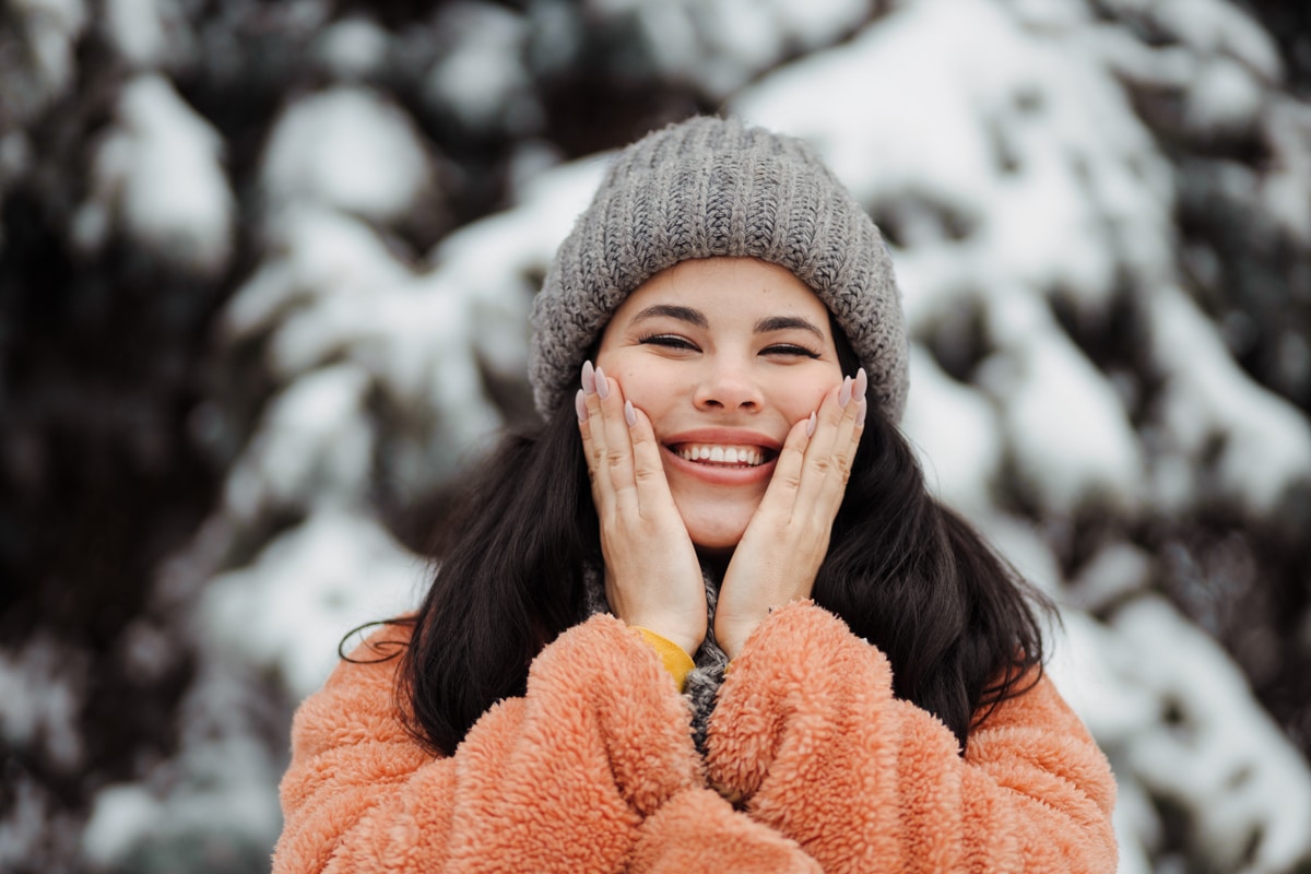 Woman smiles and places hands on face in wintertime